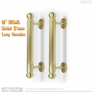 May include: Two 10-inch solid brass long door handles with rounded ends. The handles are mounted on a white wall.