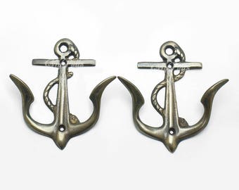 Può includere: Due ganci ad ancora in metallo dorato antico con dettagli in corda. I ganci sono montati su uno sfondo bianco.