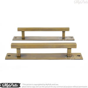 Puede incluir: Dos tiradores de puerta de armario de latón antiguo con forma rectangular. Los tiradores están montados sobre una base rectangular.