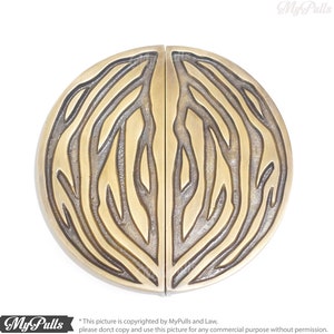 May include: A pair of round, brass door pulls with a detailed, etched design of branches and leaves. The pulls are split in half, with each half featuring a symmetrical design.