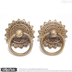 May include: Two ornate brass cabinet pulls with a ring handle and a sunflower design. The pulls have a detailed, intricate design with concentric circles and a raised center.