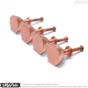 May include: Four rose gold cabinet knobs with a hexagonal shape and a screw on the back.