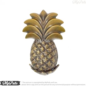 Może przedstawiać: Złoty klamka do drzwi w kształcie ananasa z detalicznym wzorem. Ananas to popularny owoc tropikalny i symbol gościnności.