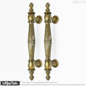 May include: Two antique brass door handles with ornate designs. The handles are long and slender with a rounded top and a decorative base.