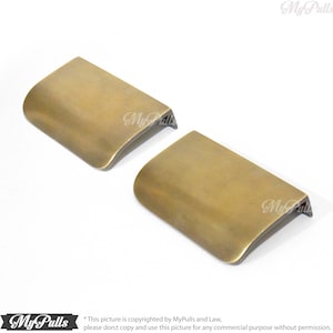May include: Two antique brass cabinet pulls with a curved edge. The pulls are approximately 3 inches long and 1 inch wide.