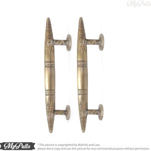 Könnte beinhalten: Zwei verzierte Türgriffe aus Messing mit aufwendigen Designs. Die Griffe sind lang und schlank mit einer spitzen Spitze. Sie haben einen traditionellen, dekorativen Stil.