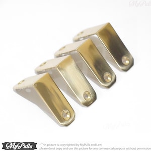 Puede incluir: Cuatro soportes de esquina de metal de color dorado con bordes redondeados y un solo agujero en cada soporte.