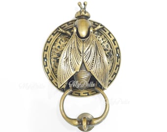 May include: A brass door knocker shaped like a bee with intricate details. The bee is mounted on a round plate with a decorative border. The knocker has a ring for pulling.