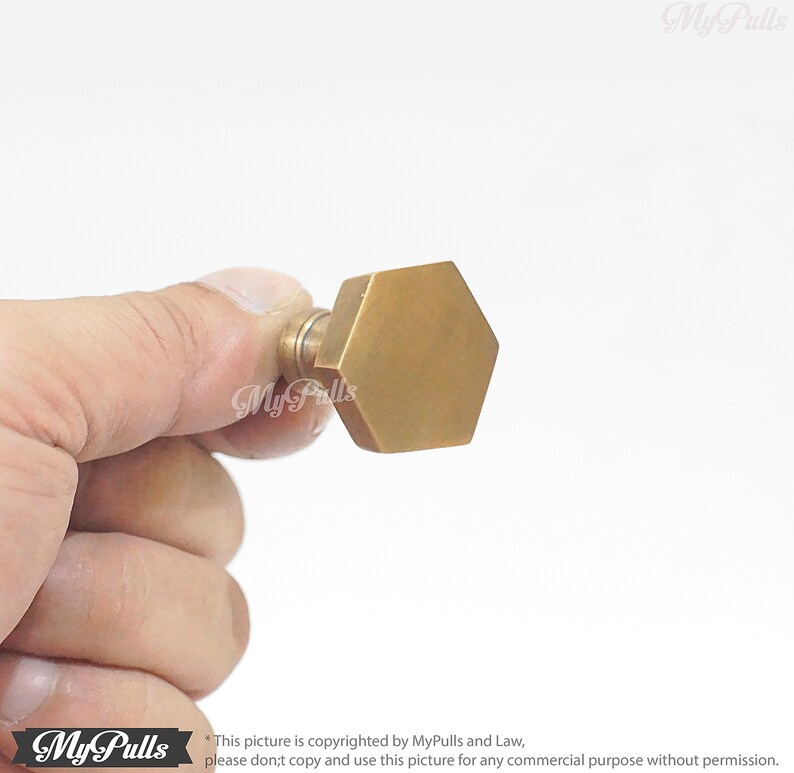 Puede incluir: Un pomo de armario hexagonal dorado con una superficie lisa.