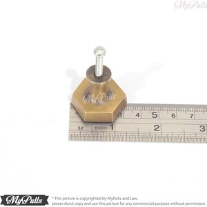 Puede incluir: Un pomo hexagonal de lat&oacute;n para armario con un tornillo, que mide 2,5 cm de di&aacute;metro. El pomo se muestra junto a una regla para referencia de tama&ntilde;o.