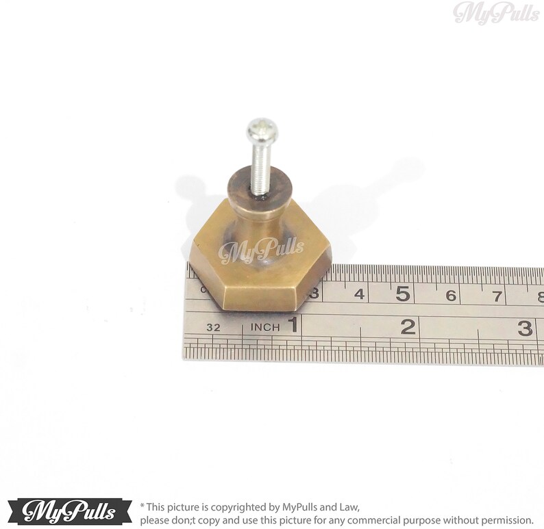 Puede incluir: Un pomo hexagonal de lat&oacute;n para armario con un tornillo, que mide 2,5 cm de di&aacute;metro. El pomo se muestra junto a una regla para referencia de tama&ntilde;o.