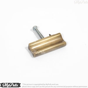May include: A brass cabinet pull with a rectangular shape and a slightly curved top. The pull has a brushed finish and a single screw hole.