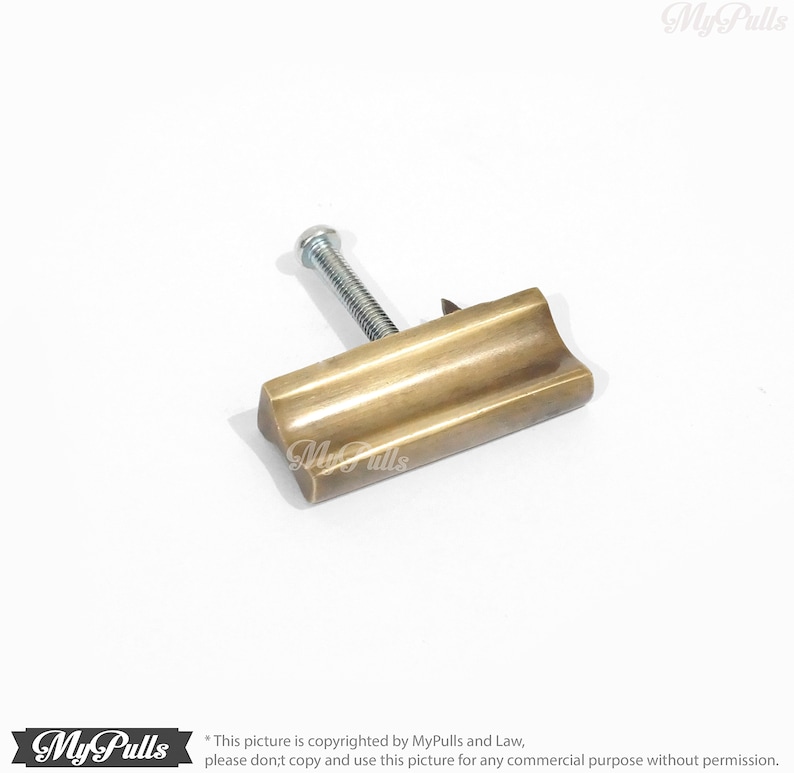 May include: A brass cabinet pull with a rectangular shape and a slightly curved top. The pull has a brushed finish and a single screw hole.
