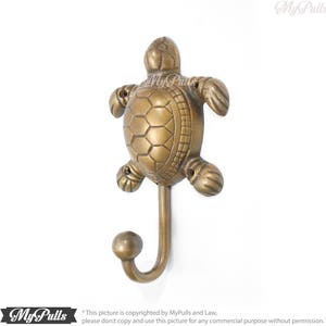 May include: A brass turtle hook with a detailed shell design. The hook is in the shape of a turtle with its head turned to the side. The hook is a decorative and functional piece for a bathroom or bedroom.