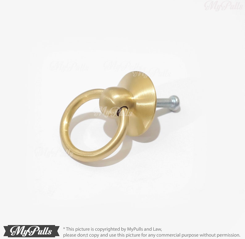 Puede incluir: Una manija de puerta de armario de anillo dorado con un anillo redondo y una base plana. La manija est&aacute; unida a un tornillo.