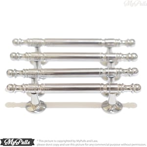 May include: Four silver cabinet pulls with a decorative design. Each pull has a round knob on each end and a decorative pattern in the middle.