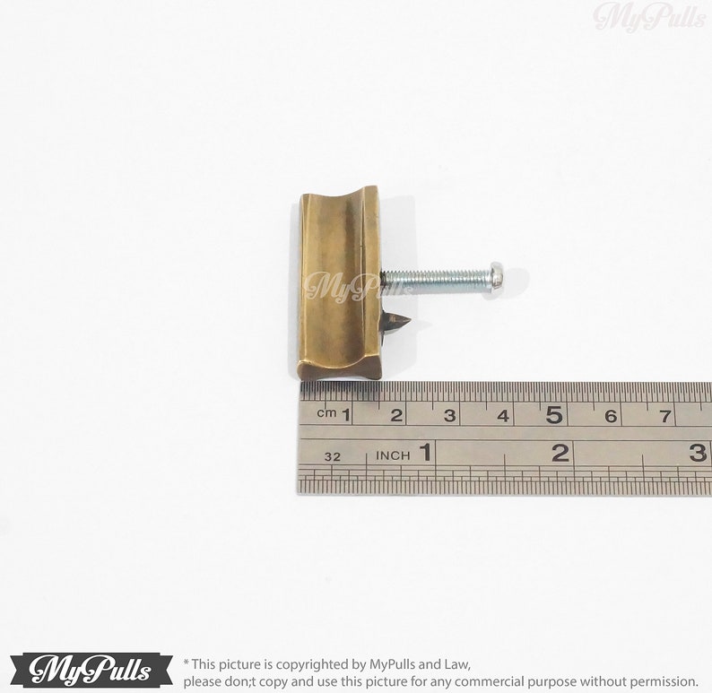 May include: A brass cabinet pull with a curved design and a screw. The pull is 2.5 cm long.