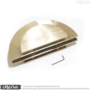 May include: Three stacked, half-circle, brass cabinet pulls with a brushed finish. The pulls are designed to be mounted on a cabinet door or drawer. A small, black Allen wrench is included for installation.