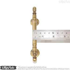 Pode incluir: Um puxador de arm&aacute;rio de cor lat&atilde;o com um design cil&iacute;ndrico, com aproximadamente 7,6 cm de comprimento. O puxador tem uma base redonda e um topo decorativo. Uma r&eacute;gua &eacute; colocada ao lado do puxador para medi&ccedil;&atilde;o.