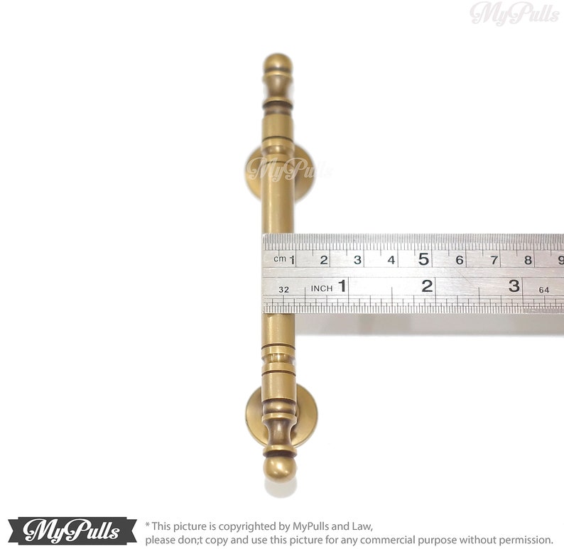 Pode incluir: Um puxador de arm&aacute;rio de cor lat&atilde;o com um design cil&iacute;ndrico, com aproximadamente 7,6 cm de comprimento. O puxador tem uma base redonda e um topo decorativo. Uma r&eacute;gua &eacute; colocada ao lado do puxador para medi&ccedil;&atilde;o.