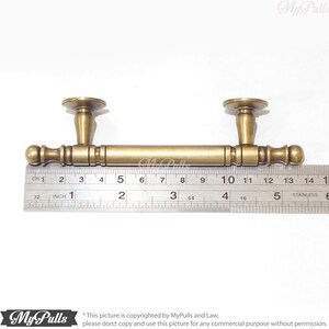 Pode incluir: Um puxador de arm&aacute;rio em tom de lat&atilde;o com uma barra e dois postes decorativos. O puxador mede aproximadamente 14 cm de comprimento. O design inclui uma barra cil&iacute;ndrica com detalhes decorativos e extremidades arredondadas. Os postes t&ecirc;m uma base circular e uma forma c&oacute;nica.