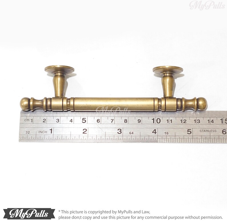 Pode incluir: Um puxador de arm&aacute;rio em tom de lat&atilde;o com uma barra e dois postes decorativos. O puxador mede aproximadamente 14 cm de comprimento. O design inclui uma barra cil&iacute;ndrica com detalhes decorativos e extremidades arredondadas. Os postes t&ecirc;m uma base circular e uma forma c&oacute;nica.