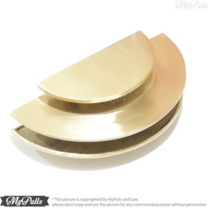 May include: A set of three gold-toned, half-circle cabinet pulls. The pulls are stacked on top of each other, with the largest pull on the bottom and the smallest pull on the top.