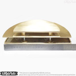 May include: A set of three brass door pulls, each with a rounded, semi-circular shape. The pulls are stacked on top of each other, with the largest pull on the bottom and the smallest pull on the top. The pulls are approximately 18 inches wide.