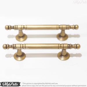 May include: Two antique brass cabinet pulls. Each pull features a cylindrical bar with decorative end pieces and a flared base. The pulls are shown against a white background. The text "My Pulls" is visible on the image.