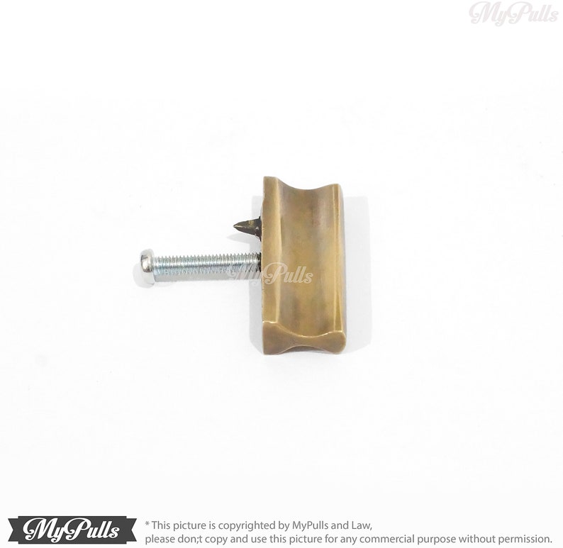May include: A brass cabinet pull with a curved rectangular shape and a screw.