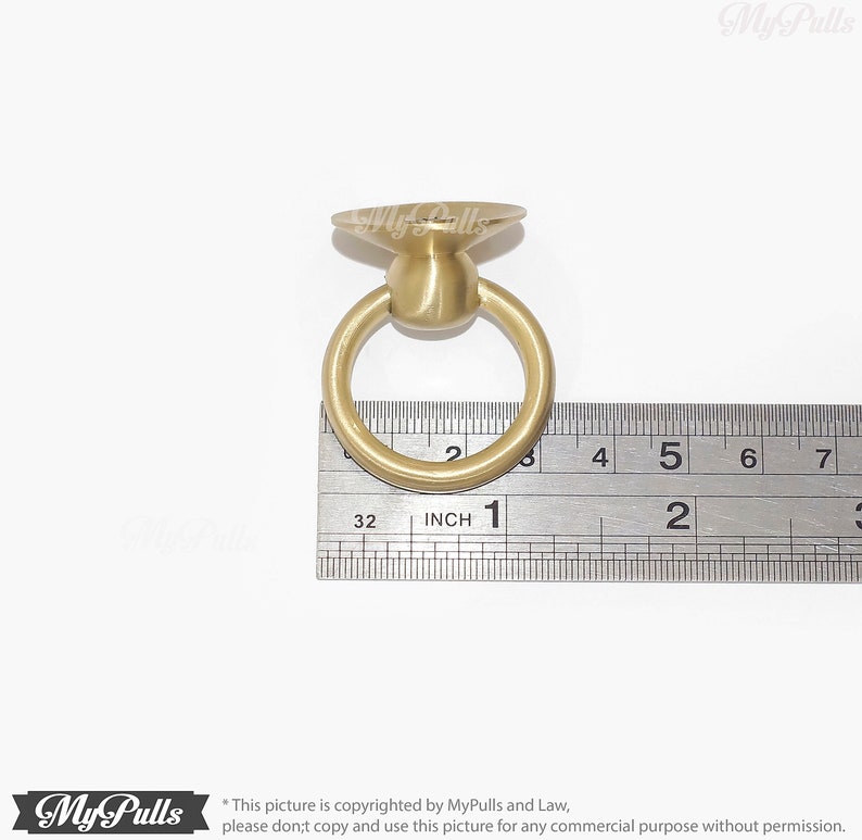 Puede incluir: Un tirador de anillo de metal dorado con una parte superior plana y circular. El anillo tiene un di&aacute;metro de aproximadamente 2,5 cm. Se muestra una regla para la escala.