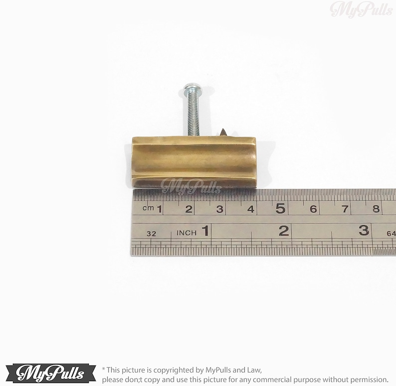 May include: A gold-toned metal cabinet knob with a square shape and a raised centre. The knob is attached to a screw and measures approximately 2.5 cm in length.