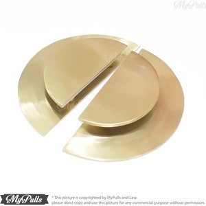 May include: A pair of gold-toned half-circle door pulls. The pulls are designed to be installed on a door, with one half on each side of the door. The pulls are made of metal and have a smooth, polished finish.
