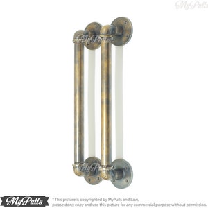 May include: Two antique brass industrial style door pulls with a pipe design. The pulls are mounted to a wall with round flanges.
