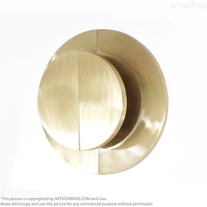 May include: A circular wall sculpture made of brass with a layered design. The sculpture has a smooth, polished finish and a warm, golden color.