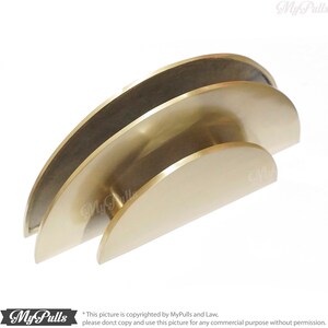 May include: Two gold-toned metal half-circle cabinet pulls, stacked on top of each other. The pulls are smooth and have a rounded edge.