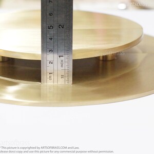 May include: Two round, brass, decorative plates, one stacked on top of the other. The top plate is slightly smaller than the bottom plate. Both plates have a smooth, polished surface. A ruler is placed next to the plates, showing that the top plate is approximately 1 inch in diameter.