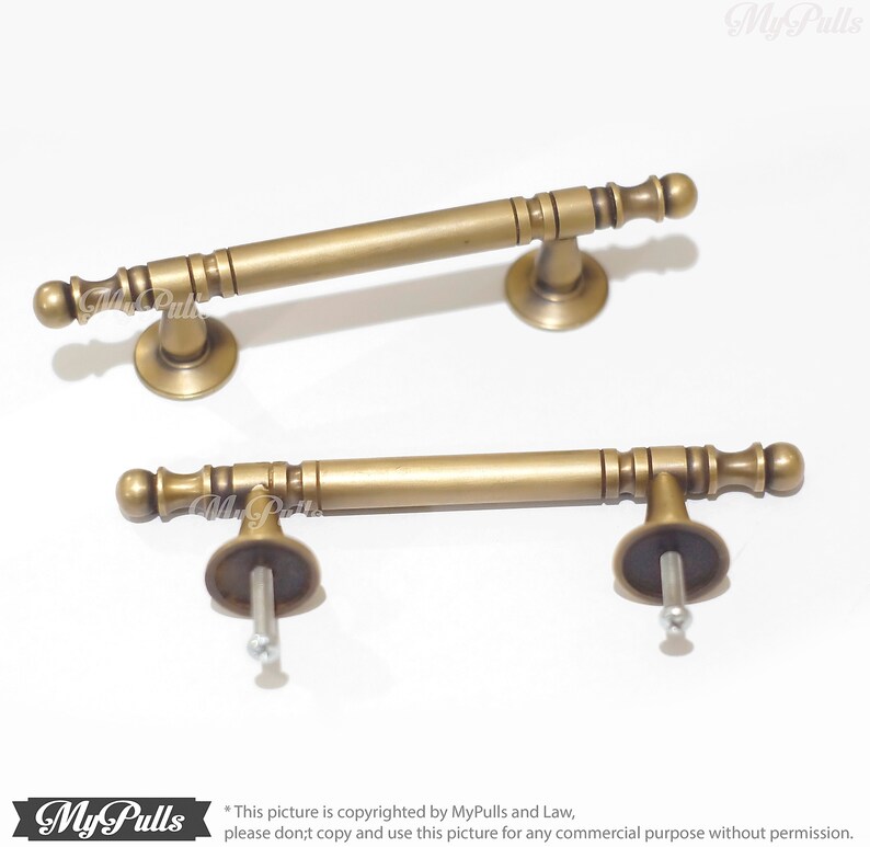 Pode incluir: Duas puxadores de arm&aacute;rio de lat&atilde;o antigo. Cada puxador tem uma barra cil&iacute;ndrica com detalhes decorativos e extremidades arredondadas. Os puxadores s&atilde;o montados em uma base circular com um parafuso para instala&ccedil;&atilde;o. Fundo branco.