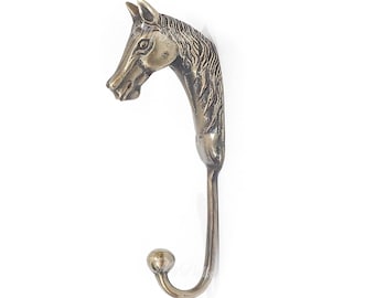 May include: A brass horse head coat hook with a detailed design. The hook is curved and has a rounded end.