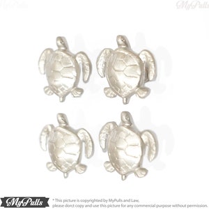 Könnte beinhalten: Vier silberne Schildkröten-Schubladengriffe. Die Schildkröten sind nach vorne gerichtet, mit erhobenem Kopf und ausgestreckten Beinen. Die Schildkröten haben eine strukturierte Schale und einen glatten Körper.