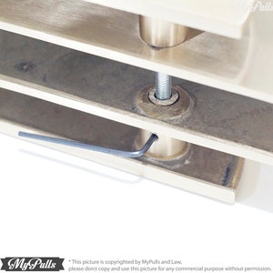 May include: Close-up of a brushed nickel door handle with a silver allen wrench inserted into the screw hole. The handle is attached to a white door frame.