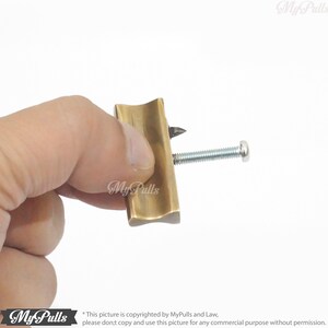 May include: A brass tool with a pointed tip and a screw. The tool is held in a hand.