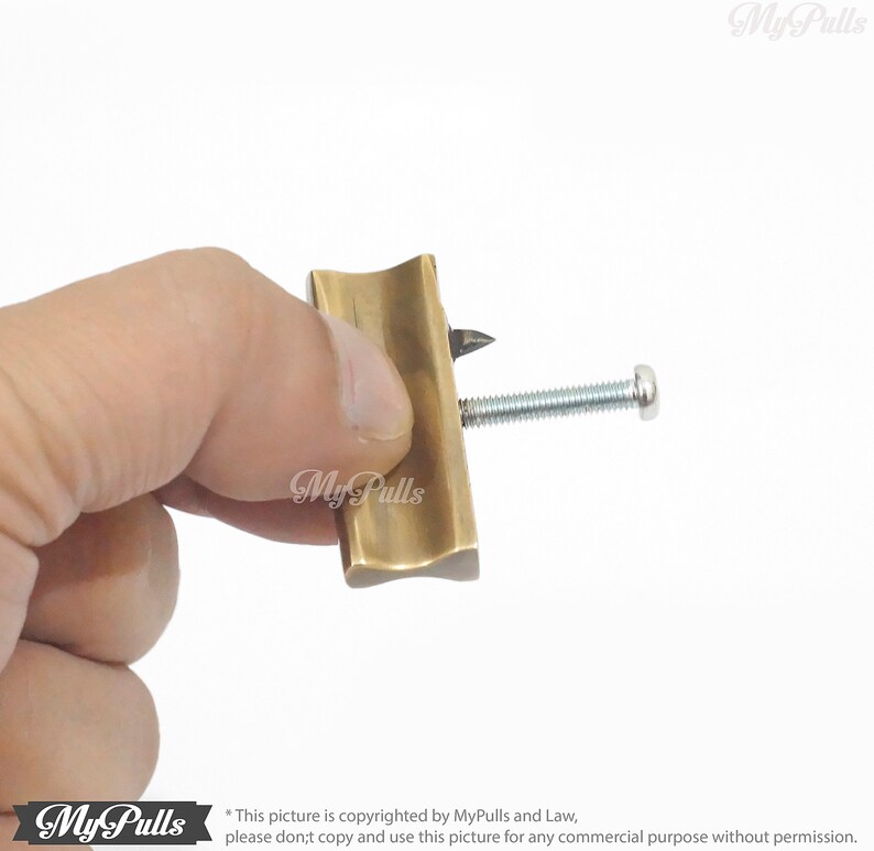 May include: A brass tool with a pointed tip and a screw. The tool is held in a hand.