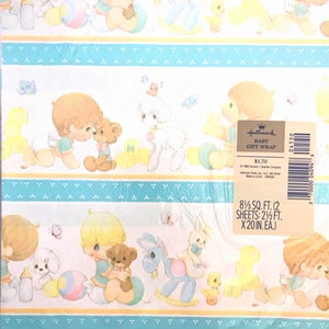 Op de afbeelding: Hallmark Baby Geschenkpapier met een blauw en geel patroon met illustraties van kinderen die met speelgoed spelen. De tekst op het etiket luidt "Hallmark Baby Geschenkpapier $ 1,70 8 1/3 sq. ft. (2 vellen: 2 1/2 ft. x 20 in. ea.)"