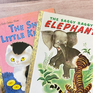 Pode incluir: Dois livros infantis vintage. O primeiro livro é rosa com um gato preto e branco na capa e o título "The Shy Little Kitten". O segundo livro é branco com um elefante cinza e um tigre listrado na capa e o título "The Saggy Baggy Elephant".