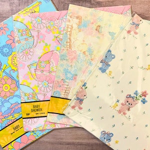 May include: Four rolls of baby shower wrapping paper. The paper features different designs including pastel blue and pink floral patterns, baby carriages, and teddy bears. The text on the paper reads "Baby Shower".