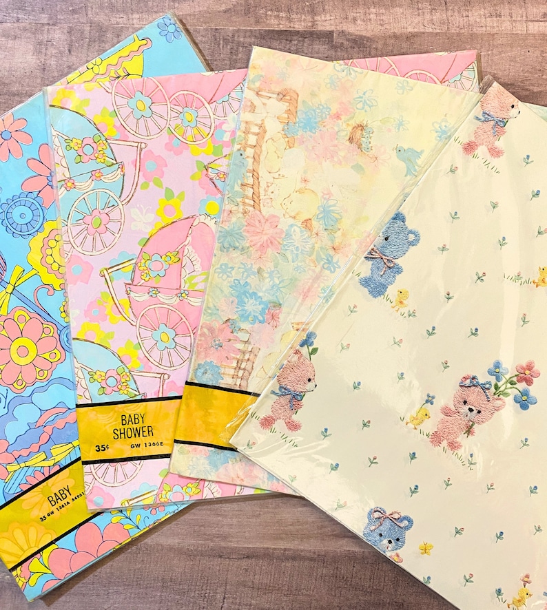 May include: Four rolls of baby shower wrapping paper. The paper features different designs including pastel blue and pink floral patterns, baby carriages, and teddy bears. The text on the paper reads "Baby Shower".