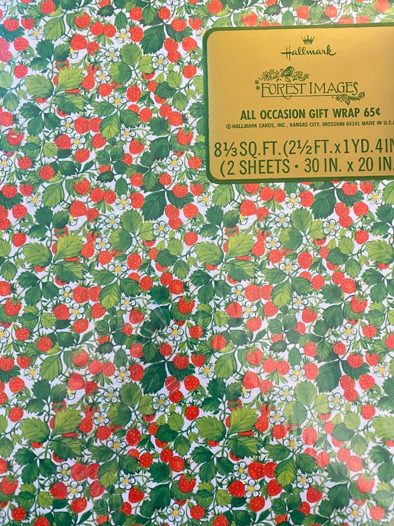 May include: A sheet of red and green strawberry patterned gift wrap with the text "Hallmark Forest Images All Occasion Gift Wrap 65&cent; Hallmark Cards, Inc. Kansas City, Missouri 64141 Made in U.S.A. 8 1/3 sq. ft. (2 1/2 ft. x 1 yd. 4 in. (2 sheets 30 in. x 20 in."