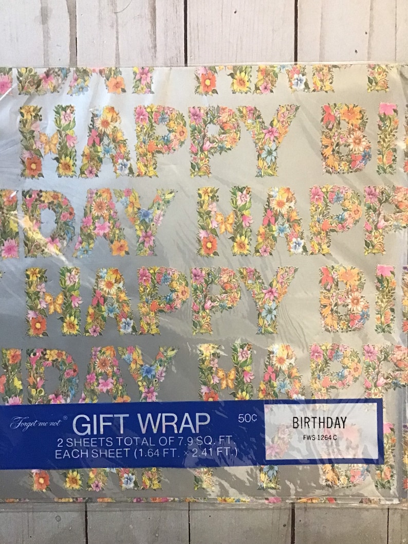 May include: A roll of floral patterned gift wrap with the words "Happy Birthday" in large letters. The wrap is silver with a floral design in pink, yellow, and green. The text on the label reads "Forget me not Gift Wrap 2 sheets total of 7.9 sq. ft. Each sheet (1.64 ft. x 2.41 ft.) 50c Birthday FWS 1264 C".