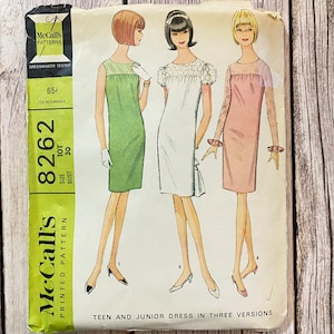 Op de afbeelding: Vintage McCall's naaipatroon voor een tiener- en juniorjurk in drie uitvoeringen. Het patroonnummer is 8262, maat 10T, borstomvang 30. Het patroon toont drie modellen die verschillende versies van de jurk dragen: groen, wit en roze.